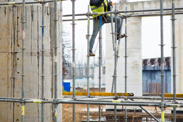 Construction worker climbs up the scaffolding at a construction site