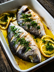 Roast dorada with lemon and rosemary in cooking pan on wooden table

