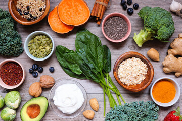 Group of healthy food ingredients. Overhead view table scene on a wooden background. Super food concept with green vegetables, berries, whole grains, seeds, spices and nutritious items.