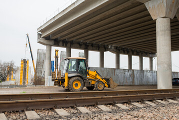 A construction excavator passes under a reinforced concrete road bridge under construction
