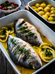 Roast dorada with lemon ,rosemary and potatoes in cooking pan on wooden table
