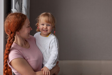 red-haired woman smiles holding a happy baby blonde with blue eyes who smiles