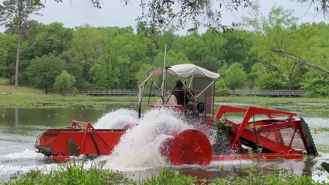 City worker operates amphibious tractor to dredge local pond of weeds