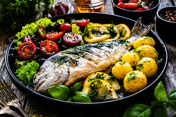 Roast dorada with potatoes and vegetables on wooden table
