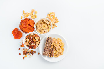 Granola bar and different types of nuts and dried fruits on a white background.