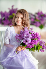 Beautiful little girl of preschool age in a delicate dress sitting on a swing decorated with flowers of lilac.