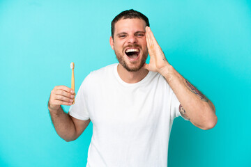 Young Brazilian man brushing teeth isolated on blue background shouting with mouth wide open