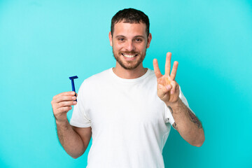 Fototapeta premium Brazilian man shaving his beard isolated on blue background happy and counting three with fingers
