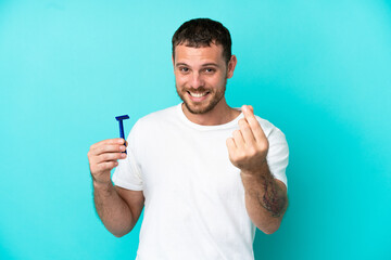 Fototapeta premium Brazilian man shaving his beard isolated on blue background making money gesture