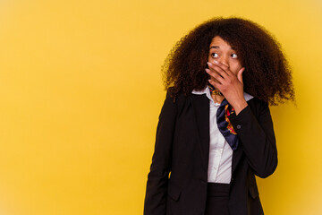 Young African American air hostess isolated on yellow background thoughtful looking to a copy space covering mouth with hand.