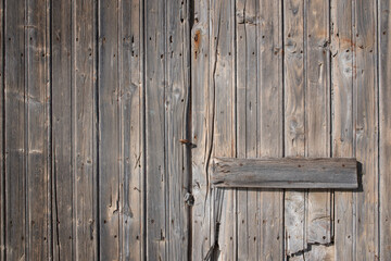 Background and detail of an old weathered closed wooden door that is in landscape format in an old wall.