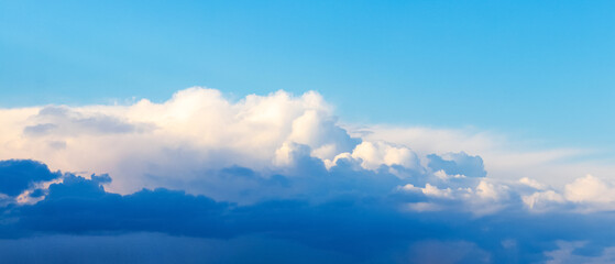 Panorama of the evening blue sky with dark and white clouds illuminated by the sun