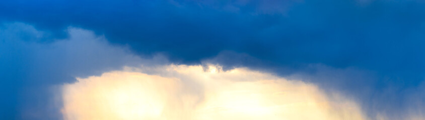Panorama of the evening blue sky with dark and light clouds illuminated by the sun