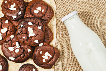 Chocolate freshly baked cookies sprinkled with almond flakes, mockup on paper notebook and burlap milk bottle background. Top view of cookies with copy space, image for banner or advertisement