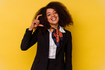 Young African American air hostess isolated on yellow background holding something little with...