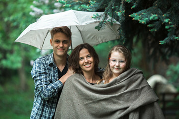 An woman with their adult son and daughter in the Park under an umbrella.