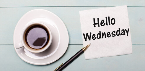 On a light blue wooden tray, there is a white cup of coffee, a handle and a napkin that says HELLO WEDNESDAY