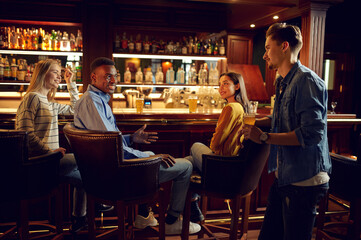 Four cheerful friends drinks beer in bar
