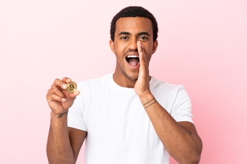 Young African American man holding a Bitcoin over isolated pink background shouting with mouth wide open