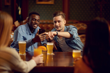 Four friends drinks alcohol at the table in bar