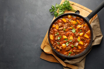 Goulash, beef stew with vegetables in tomato sauce. Top view. Dark (black) background. - obrazy, fototapety, plakaty