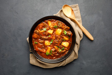Goulash, beef stew with vegetables in tomato sauce. Top view. Dark (black) background.