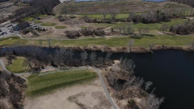 Aerial push forward over a golf course driving range, headed toward a solar array on one side of the course. Drone. Widow's Walk. Scituate.