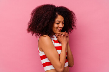 Young african american woman isolated on pink background keeps hands under chin, is looking happily aside.
