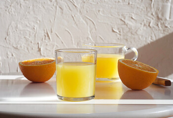 Two glasses of orange juice are on the table. Nearby are fresh oranges and a knife. Sunny day.