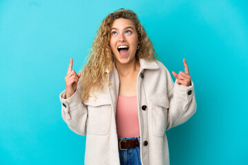 Young blonde woman isolated on blue background surprised and pointing up