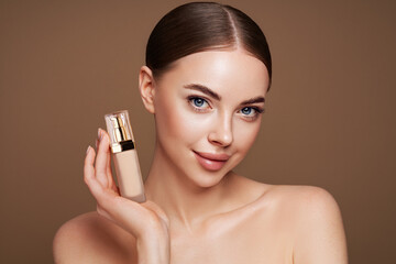 Portrait beautiful young woman with clean fresh skin. Model with foundation makeup bottle. Cosmetology, beauty and spa