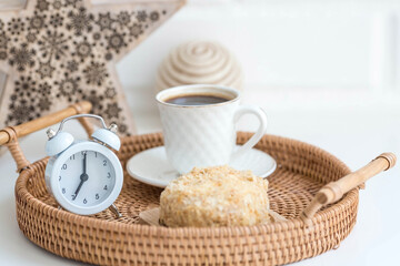 A white retro alarm clock, a cake and a cup of coffee against a white brick wall. The concept of...