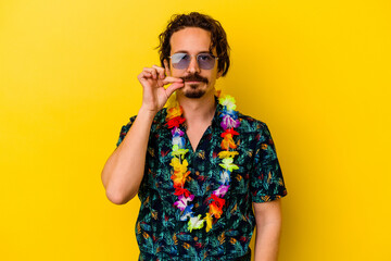 Young caucasian man wearing a hawaiian necklace isolated on yellow background with fingers on lips keeping a secret.