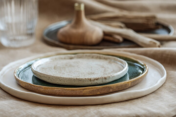 Table setting with Handmade craft plates on linen tablecloth and wood accessories in earth tones
