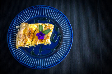 Homemade pie with cheese and eggs, honey and dahlia leaves in a dark blue plate. Bulgarian pie. Breakfast and lunch.
