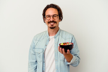 Young caucasian man eating a ramen isolated on white background happy, smiling and cheerful.