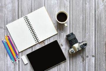 Still life, business or traveler memo concept, Top view image of open notebook with vintage camera coffee colorful pencil and tablet with blank pages on old brown wooden background, for adding text
