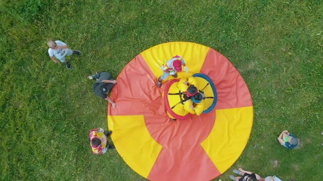 Professional sumo wrestlers in special costumes fight in red yellow circle surrounded by people on green meadow upper view