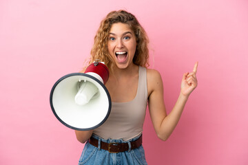 Young blonde woman isolated on pink background shouting through a megaphone and pointing side