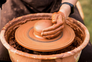 Close-up view of man working on pottery wheel and making clay pot outdoor, selective focus
