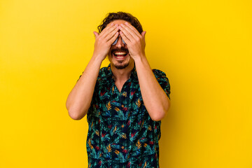 Young caucasian man wearing summer clothes isolated on yellow background covers eyes with hands, smiles broadly waiting for a surprise.