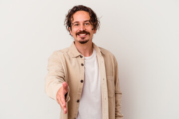 Young caucasian man isolated on white background stretching hand at camera in greeting gesture.