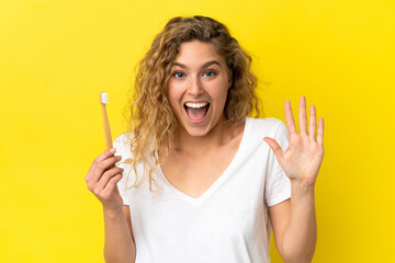 Young caucasian woman holding a brushing teeth isolated on yellow background counting five with fingers