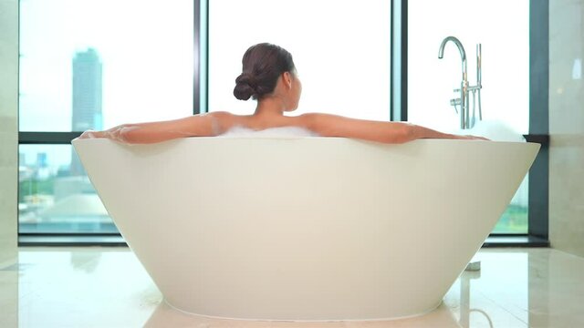Rear View of Woman in Luxurious Bathtub Enjoying City View.