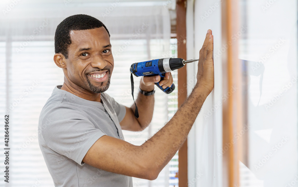 Wall mural portrait of happy african american black man using electric drill on wall. diy, do it yourself hobby