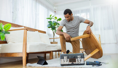 Portrait of busy African American black man screwing table with electric drill interior living...
