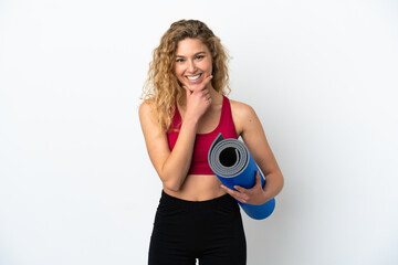 Young sport blonde woman going to yoga classes while holding a mat isolated on white background looking to the side and smiling