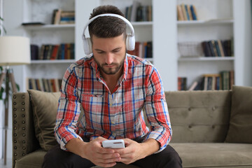 Attractive young man relaxing on a couch at home and using mobile phone for cheking social nets. © ty