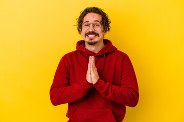 Fototapeta premium Young caucasian man isolated on yellow background holding hands in pray near mouth, feels confident.