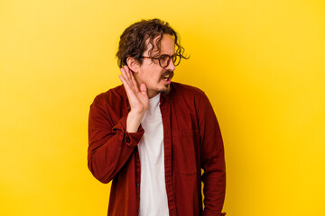 Young caucasian man isolated on yellow background trying to listening a gossip.